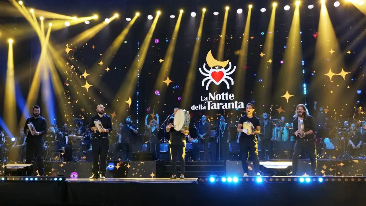 Artisti sul palco con tamburelli, orchestra e luci scintillanti per la sagra della taranta.