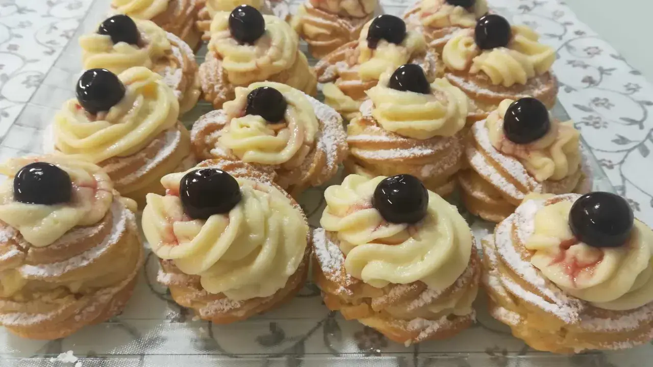 Zeppole pugliesi, dolci fritti con crema pasticcera e ciliegina, spolverati di zucchero a velo.