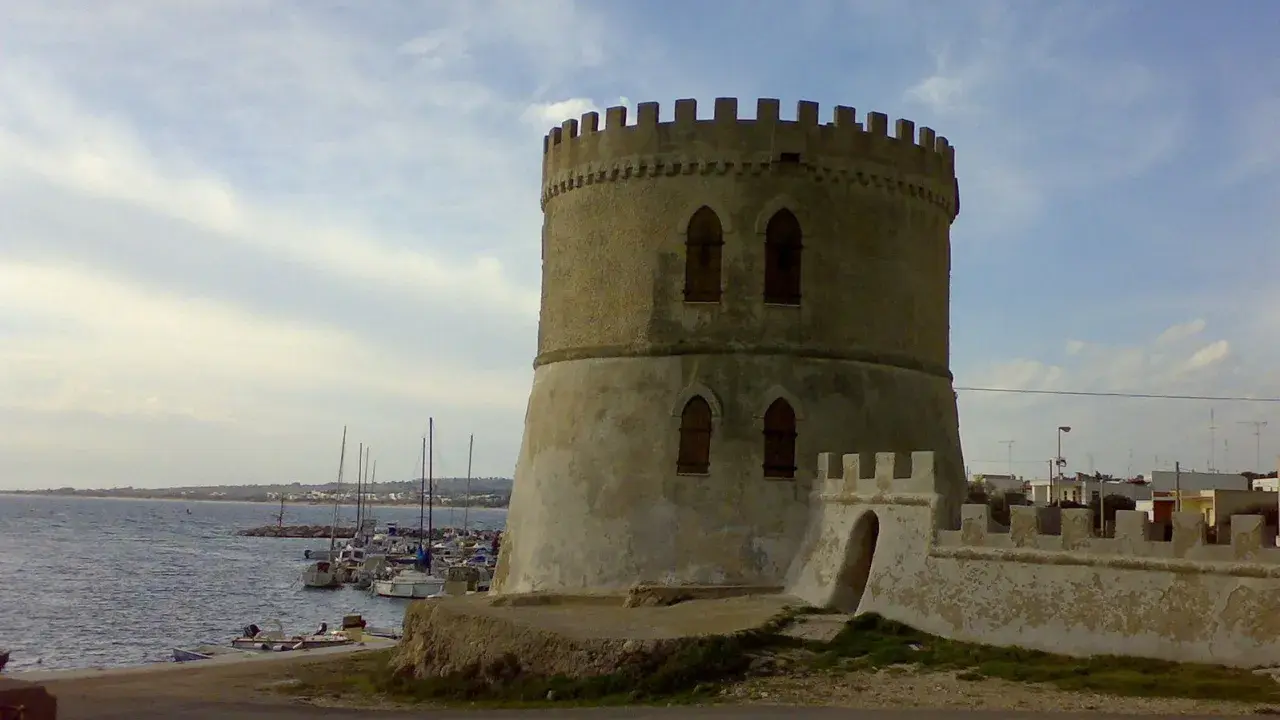 Torre Vado centro storico: antica torre circolare con merlature, affacciata sul mare con barche ormeggiate.
