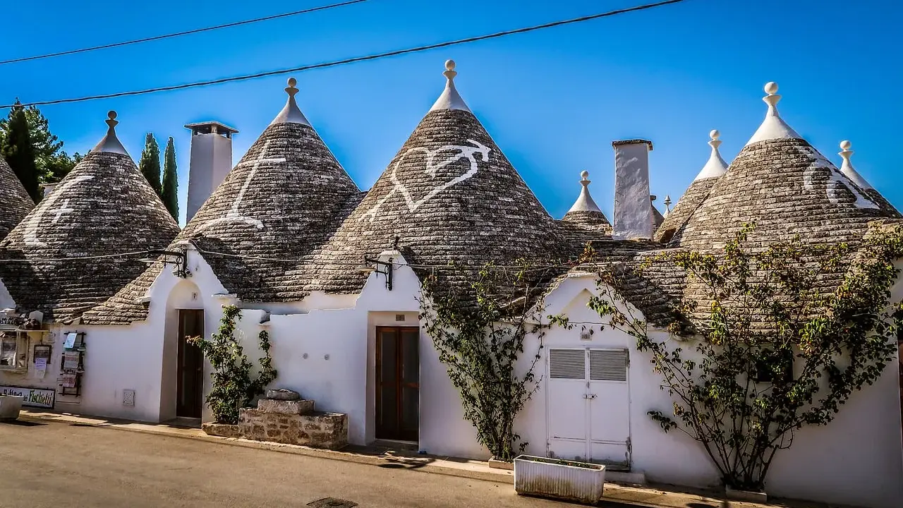 Trulli bianchi con tetti conici in pietra, un cuore disegnato su uno di essi, in un borgo tra i più belli d'Italia in Puglia.