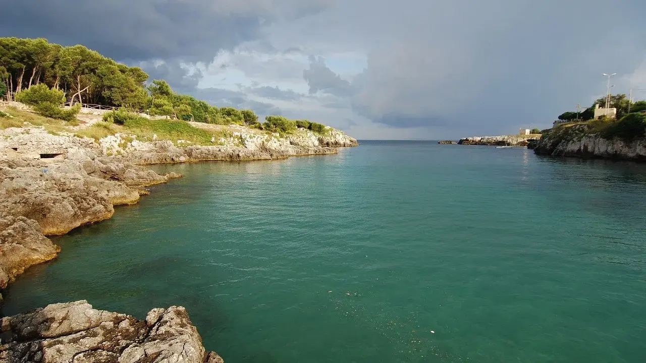 Baia rocciosa con acqua cristallina, alberi sulla costa. Un paesaggio che evoca i modi di dire salentini, come "fare la bella vita".