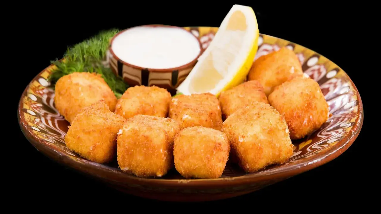 Croccanti cubetti di ricotta fritta salentina dorati, serviti su un piatto decorato con limone, salsa bianca e aneto.