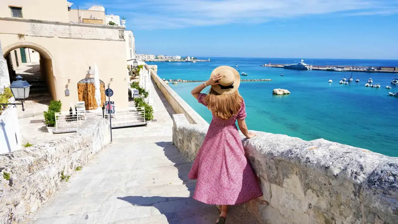 Una donna con cappello di paglia ammira il mare turchese e il porto di Otranto. Scopri cosa vedere in questo gioiello pugliese.