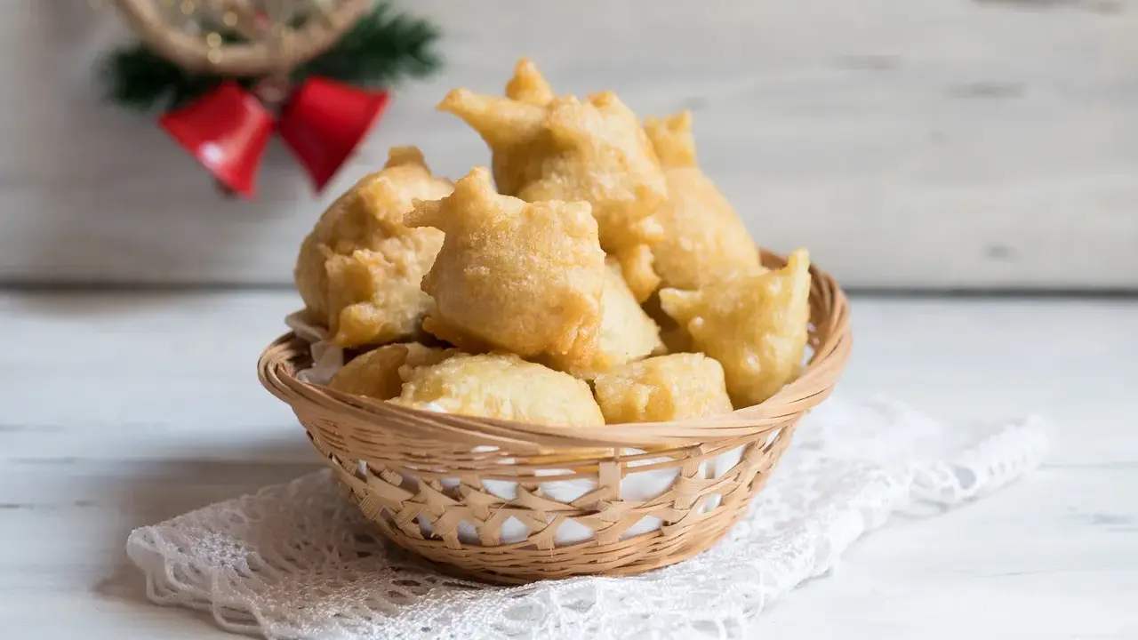 Cesto di pittula salentina dorata, un dolce fritto tipico delle feste, su un pizzo bianco.