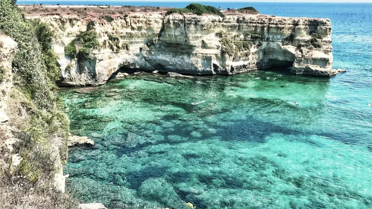 Scogliere bianche e acque cristalline, un paradiso tra le spiagge Puglia. Nuotatori si godono il mare turchese.