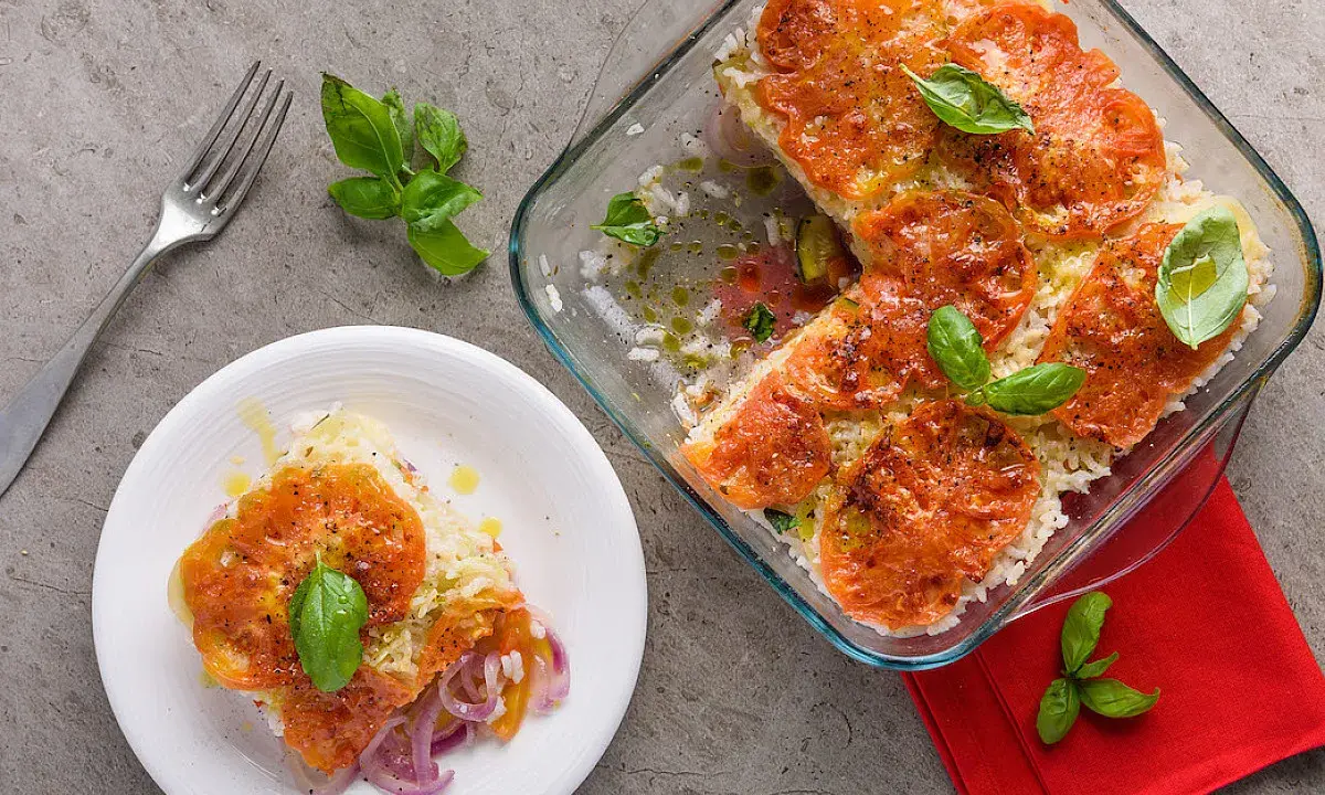 Una fetta di tiella pugliese di verdure, con riso, pomodori e cipolle rosse, guarnita con basilico fresco.