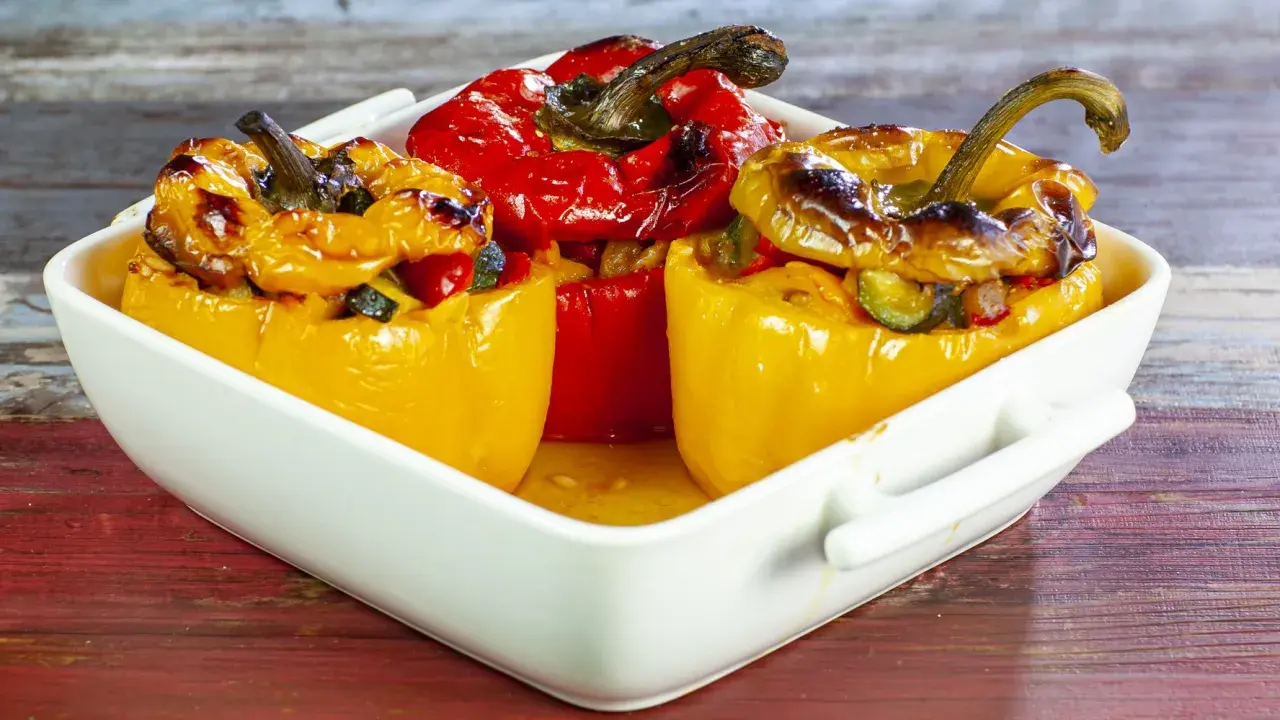 Peperoni ripieni di riso alla salentina, dorati e invitanti, in una teglia bianca su un tavolo di legno.