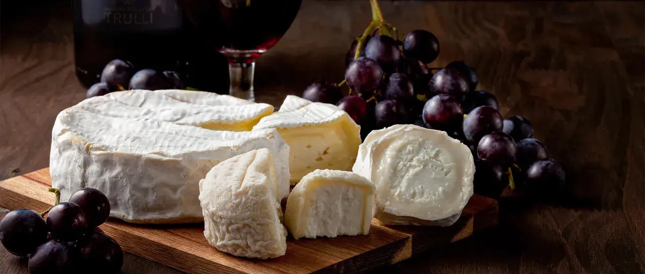 Formaggi pugliesi e uva nera, con una bottiglia di vino rosso sullo sfondo.