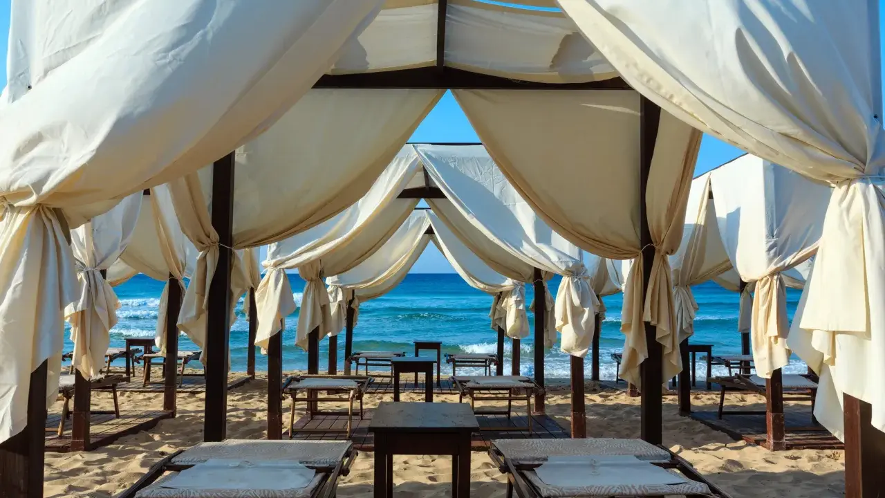 Tende bianche su una spiaggia dorata, con il mare azzurro sullo sfondo. Un angolo di paradiso che ricorda le Maldive del Salento, pronto per il relax.