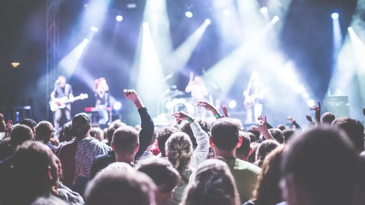 Folla entusiasta a un concerto in Puglia il 1 maggio, con luci intense e musicisti sul palco.