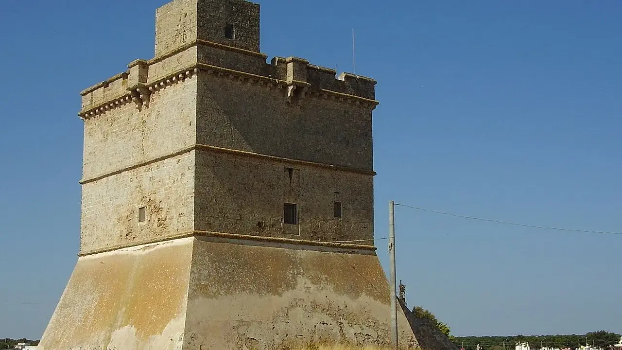Torre costiera a Sant Isidoro, Salento. Antica sentinella di pietra contro il cielo azzurro, con il mare e il borgo sullo sfondo.