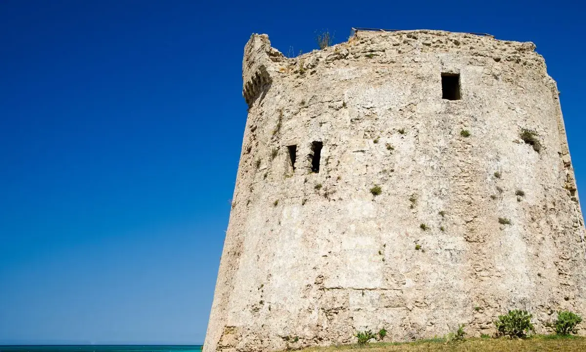 Antica torre mozza, con merli frastagliati, si erge contro un cielo blu intenso, testimone silenzioso di antiche storie.