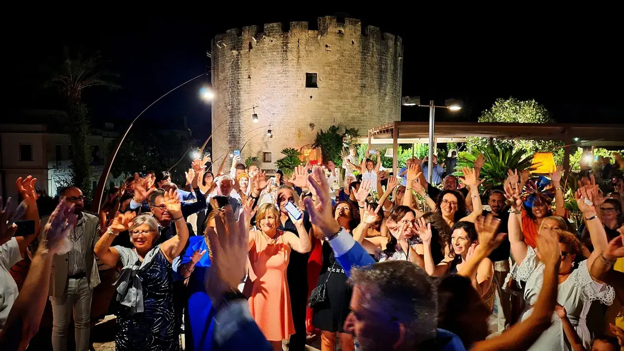 Festa con gente che alza le mani davanti a una torre antica, tipica delle sagre Salento agosto.