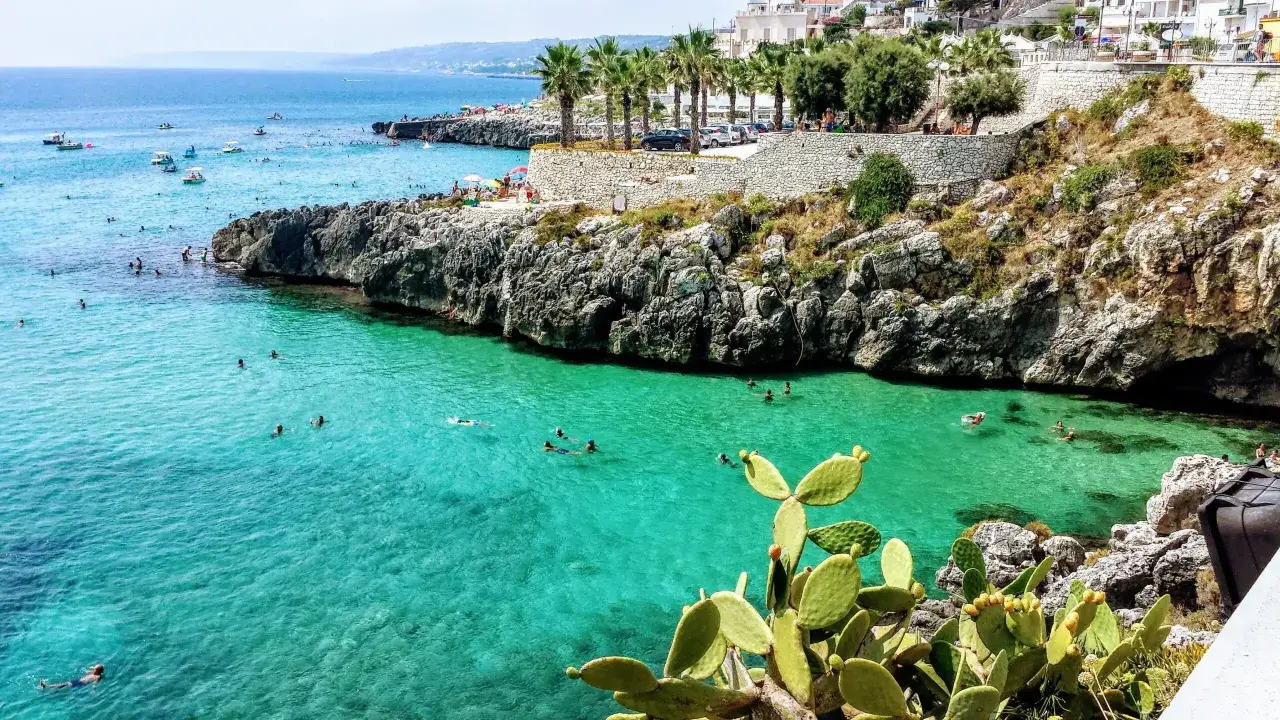 Splendida baia pugliese con acque cristalline e scogliere rocciose. Gente che nuota e si gode il sole, un vero paradiso per chi ama il **puglia mare**.