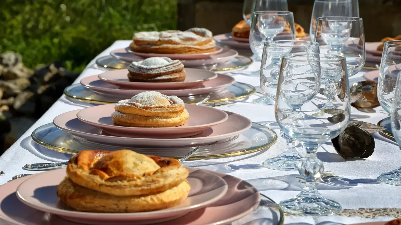 Tavola apparecchiata con bicchieri di cristallo e piatti rosa, su cui riposano dolci invitanti, tra cui una piscialetta leccese cosparsa di zucchero a velo.