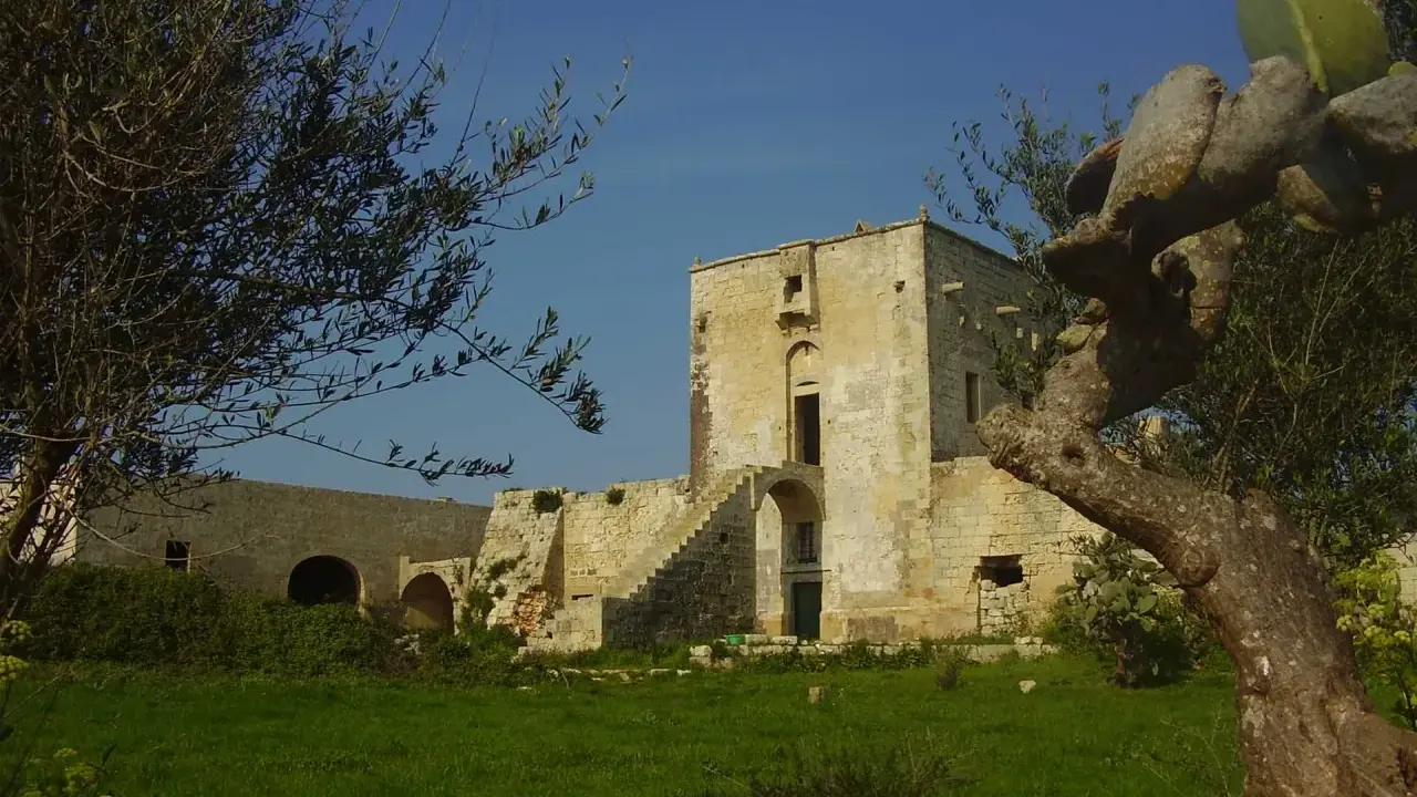 Antica masseria nella pianura salentina, con un torrione in pietra e vegetazione rigogliosa.