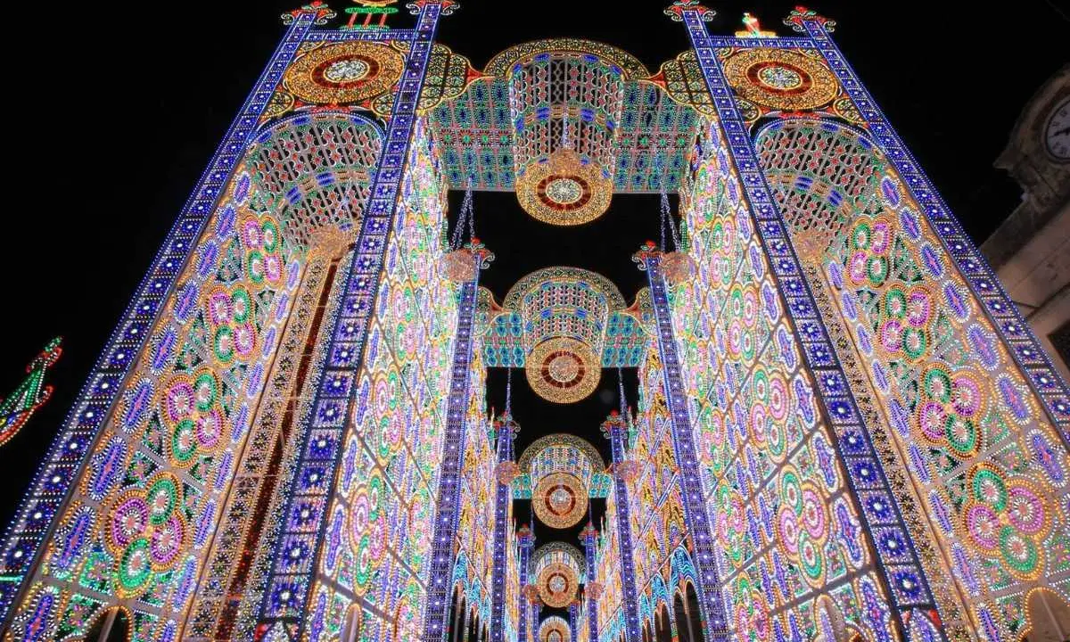 Un paese delle luminarie puglia incantato, con archi maestosi e decorazioni floreali di luci colorate che creano un tunnel magico nella notte.