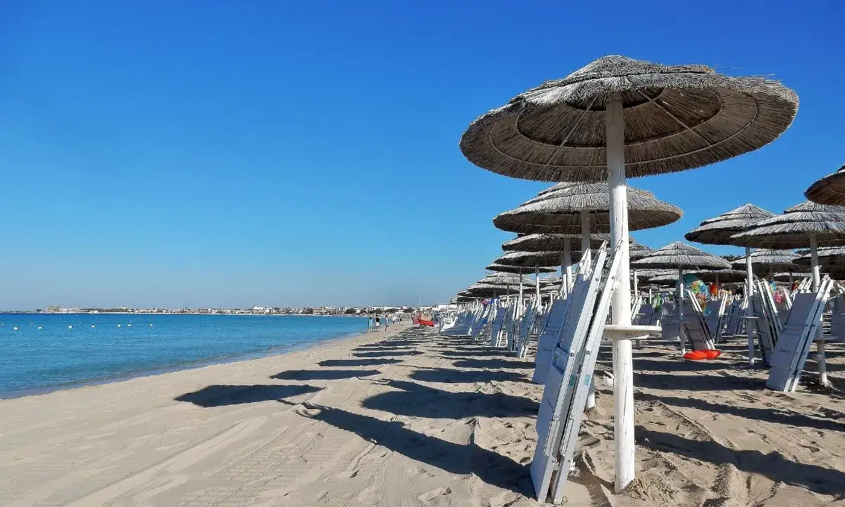 Ombrelloni di paglia e lettini bianchi sul lungomare Torre Lapillo, con il mare azzurro e il cielo limpido.