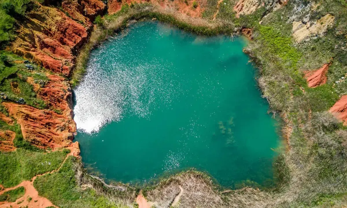 Laguna turchese in un cratere dalle rocce rosse, un paesaggio surreale delle cave di bauxite Otranto.