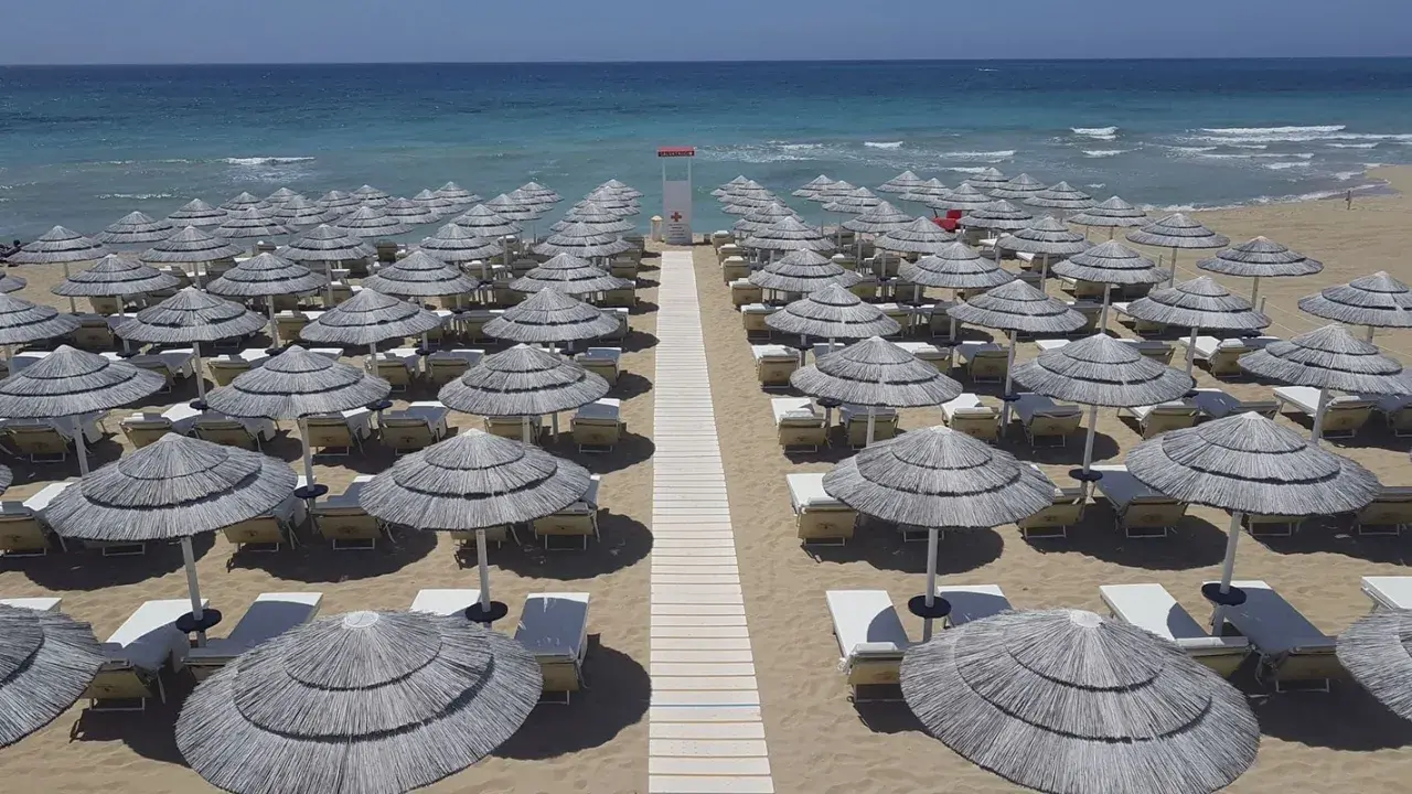 Filettato di ombrelloni di paglia e lettini sulla sabbia dorata, con il mare azzurro sullo sfondo. Un paradiso a Presicce Lido Marini.