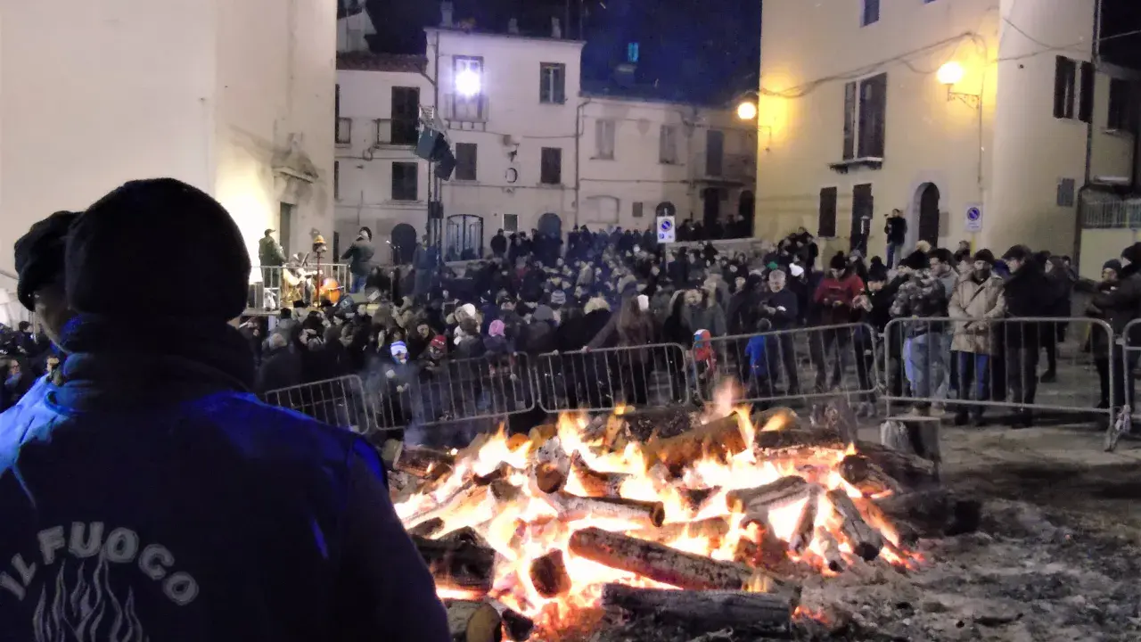 Grande falò nella piazza per la festa della birra Sant'Antonio Abate. La folla ammira le fiamme mentre un gruppo suona musica.