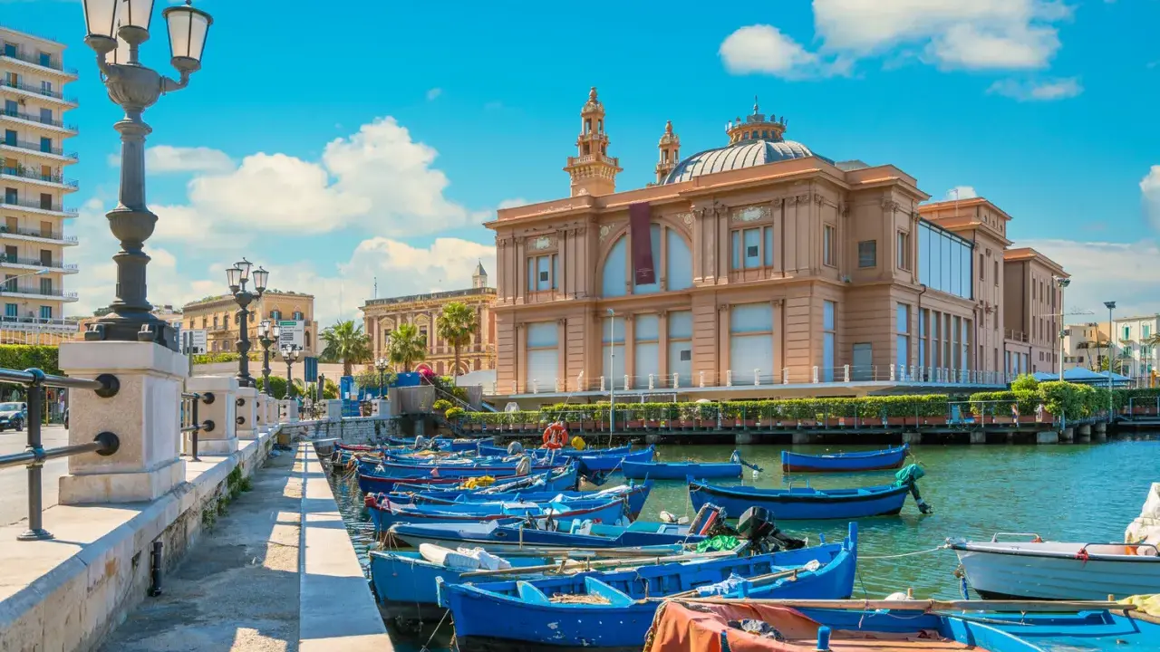 Barche blu ormeggiate nel porto di Bari, con il Teatro Margherita sullo sfondo. Un'immagine che cattura l'essenza di cosa vedere a Bari.
