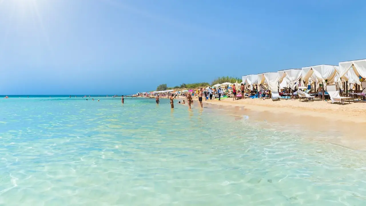 Spiaggia pugliese con acque cristalline e lettini sotto gazebo bianchi, ideale località mare Puglia per famiglie.