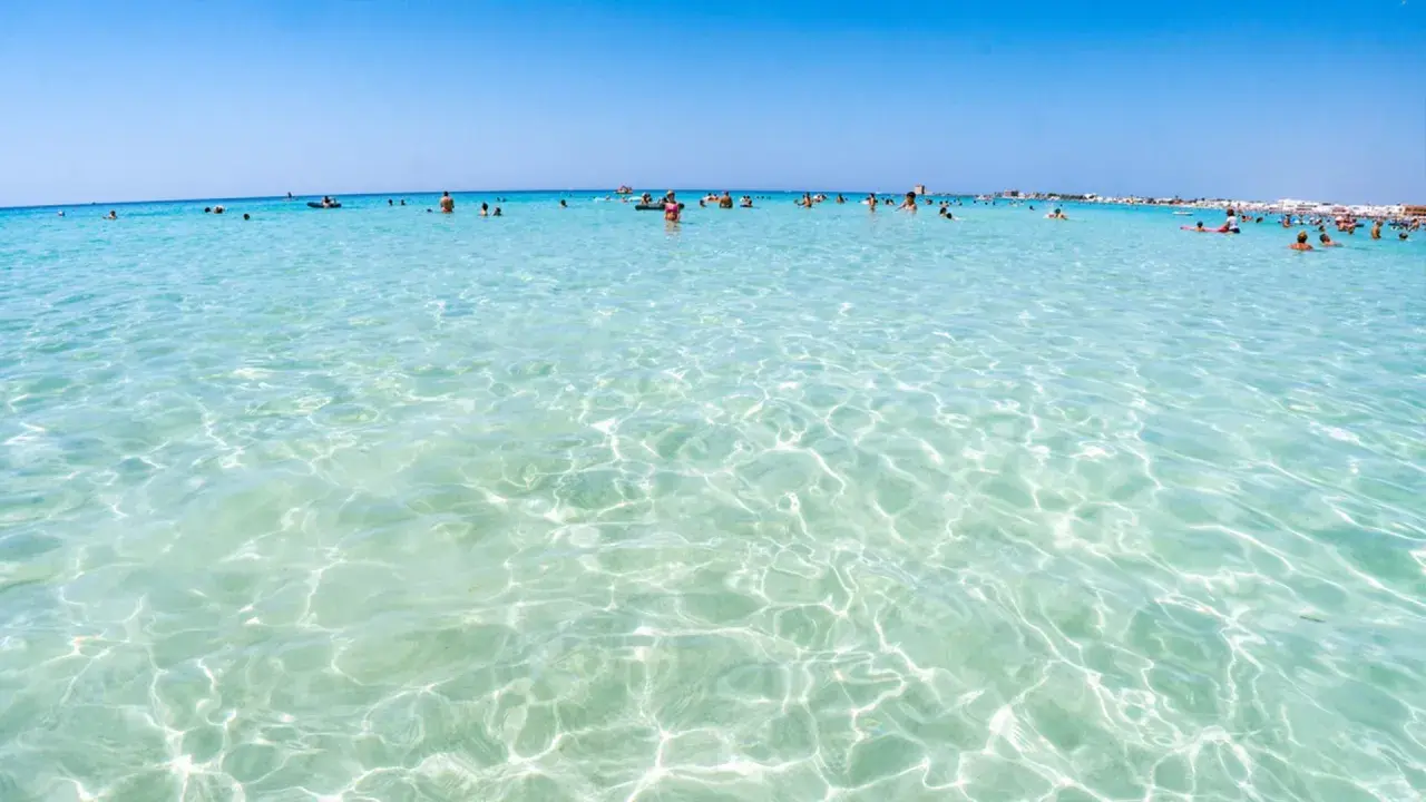 Acque cristalline e turchesi bagnano le spiagge di Lecce, dove bagnanti si godono il sole e il mare limpido.