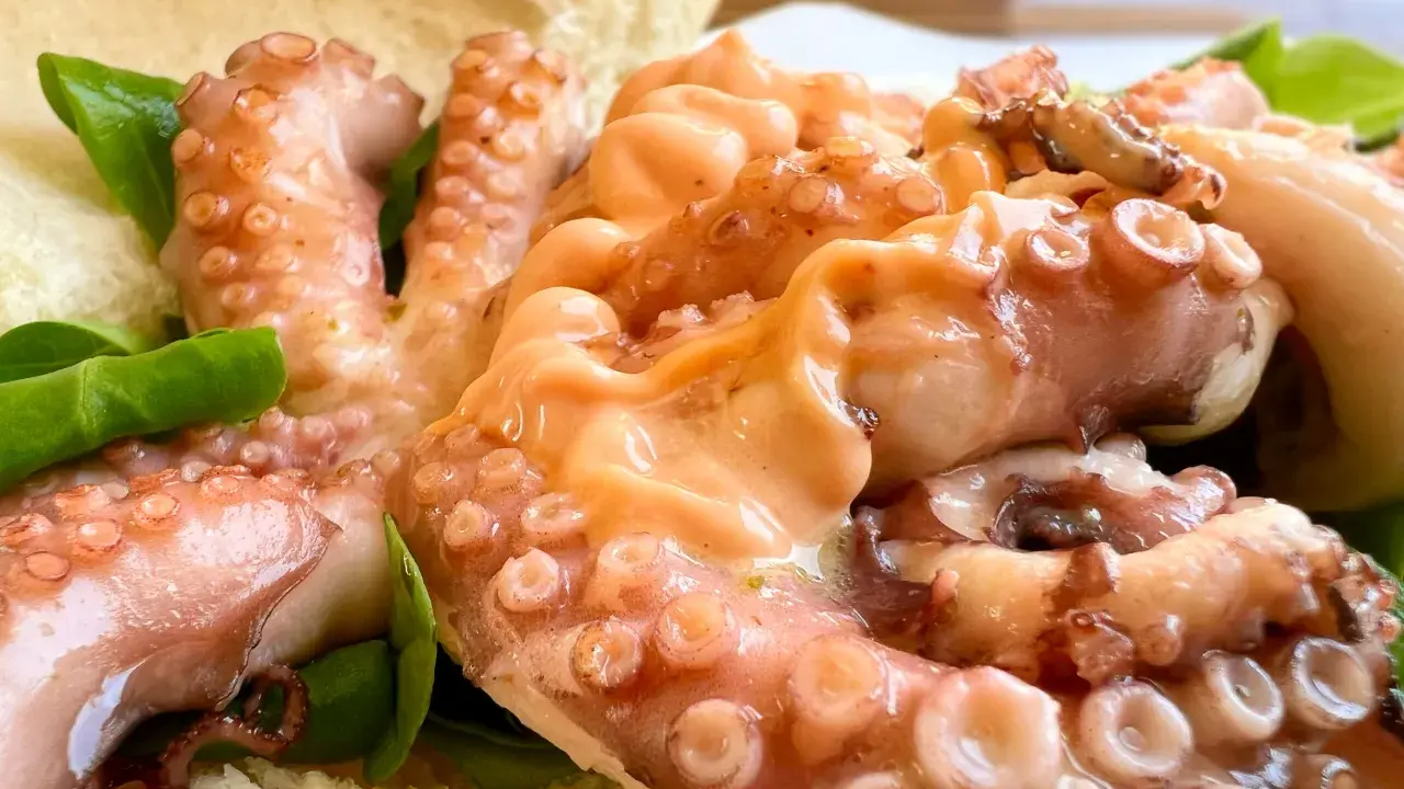 Tentacoli di polpo succulenti, un assaggio della sagra del polpo a Melendugno, serviti con pane croccante e foglie verdi.