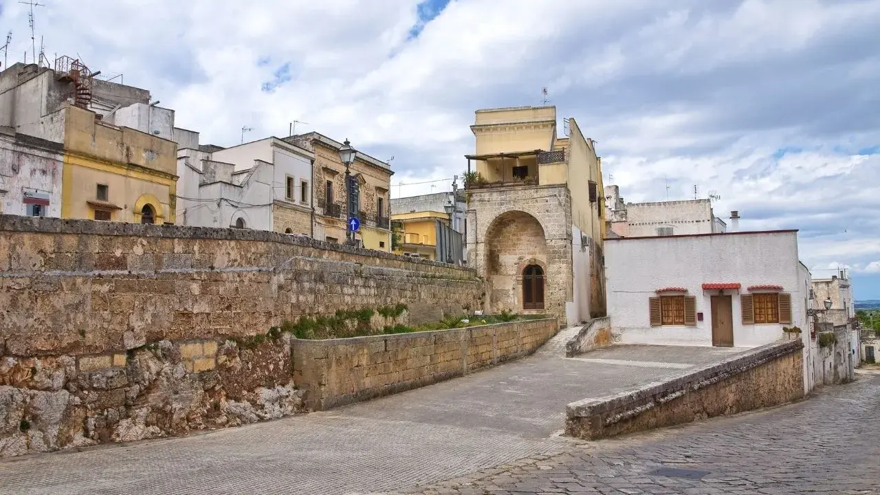 Antica strada di Ugento, dove si trova questo scorcio di case storiche con un muro in pietra grezza e un arco in tufo.