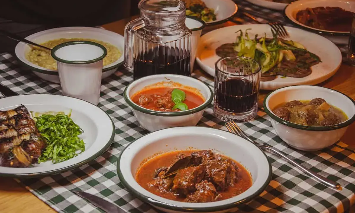 Tavola imbandita in una trattoria tipica salentina con vari piatti di carne e contorni, accompagnati da vino rosso.