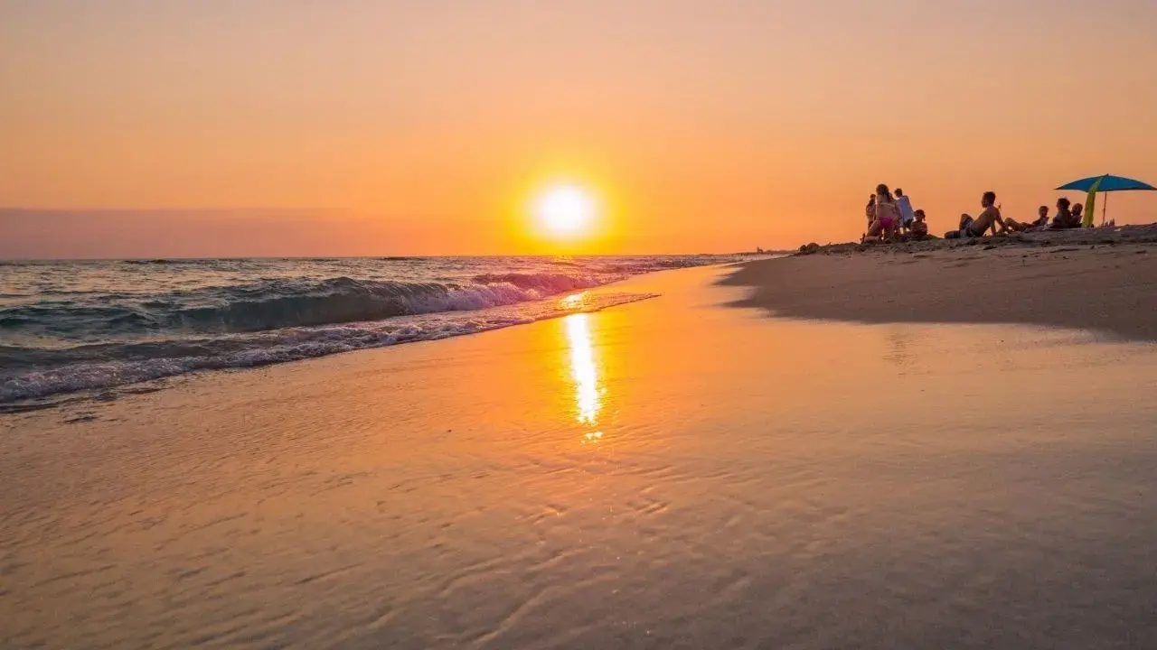 Tramonto dorato sulla spiaggia di Ugento, Salento. Famiglie rilassate sulla sabbia mentre il sole si specchia sul mare calmo.