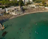 Vista aerea di una spiaggia affollata con ombrelloni e persone che nuotano nel mare cristallino, una delle spiagge più belle del mare di Taranto.