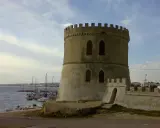 Torre Vado centro storico: antica torre circolare con merlature, affacciata sul mare con barche ormeggiate.