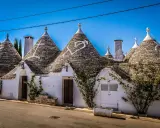 Trulli bianchi con tetti conici in pietra, un cuore disegnato su uno di essi, in un borgo tra i più belli d'Italia in Puglia.