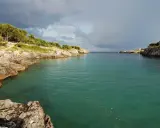 Baia rocciosa con acqua cristallina, alberi sulla costa. Un paesaggio che evoca i modi di dire salentini, come "fare la bella vita".