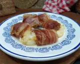 Involtini di interiora pugliesi avvolti in pancetta croccante, serviti su un piatto bianco con decorazioni blu.