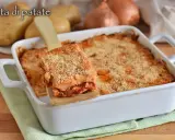 Una fetta di focaccia di patate ripiena pugliese dorata e croccante, servita da una teglia bianca.