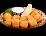 Croccanti cubetti di ricotta fritta salentina dorati, serviti su un piatto decorato con limone, salsa bianca e aneto.