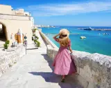 Una donna con cappello di paglia ammira il mare turchese e il porto di Otranto. Scopri cosa vedere in questo gioiello pugliese.