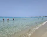 Persone in acqua cristallina vicino alla spiaggia di Gallipoli paese. Il mare calmo riflette il cielo azzurro.