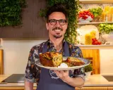 Chef sorridente con un piatto di torta salata, ispirata alle ricette leccesi, con pomodorini e basilico sullo sfondo.
