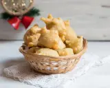 Cesto di pittula salentina dorata, un dolce fritto tipico delle feste, su un pizzo bianco.