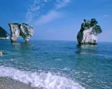 La **Baia delle Zagare** con le sue iconiche faraglioni bianchi che emergono dal mare blu intenso, sotto un cielo limpido.