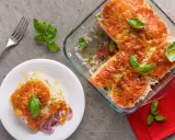 Una fetta di tiella pugliese di verdure, con riso, pomodori e cipolle rosse, guarnita con basilico fresco.