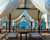 Tende bianche su una spiaggia dorata, con il mare azzurro sullo sfondo. Un angolo di paradiso che ricorda le Maldive del Salento, pronto per il relax.