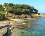 Scogliera e mare cristallino a San Gregorio, Puglia. Persone si godono il sole e l'acqua, con una scalinata che sale verso la vegetazione.