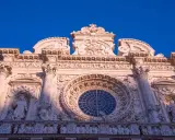 Facciata barocca di Lecce, con un grande rosone centrale e statue. Un esempio di cosa vedere a Lecce, tra arte e storia.