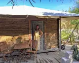 Donna sorridente in un abito a righe gialle davanti a una tenda di bambù, che incarna il glamping significato: lusso e natura.