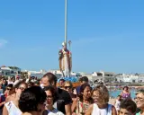 Festa San Foca: folla partecipa alla processione con la statua del santo su un carro, sotto un cielo azzurro.